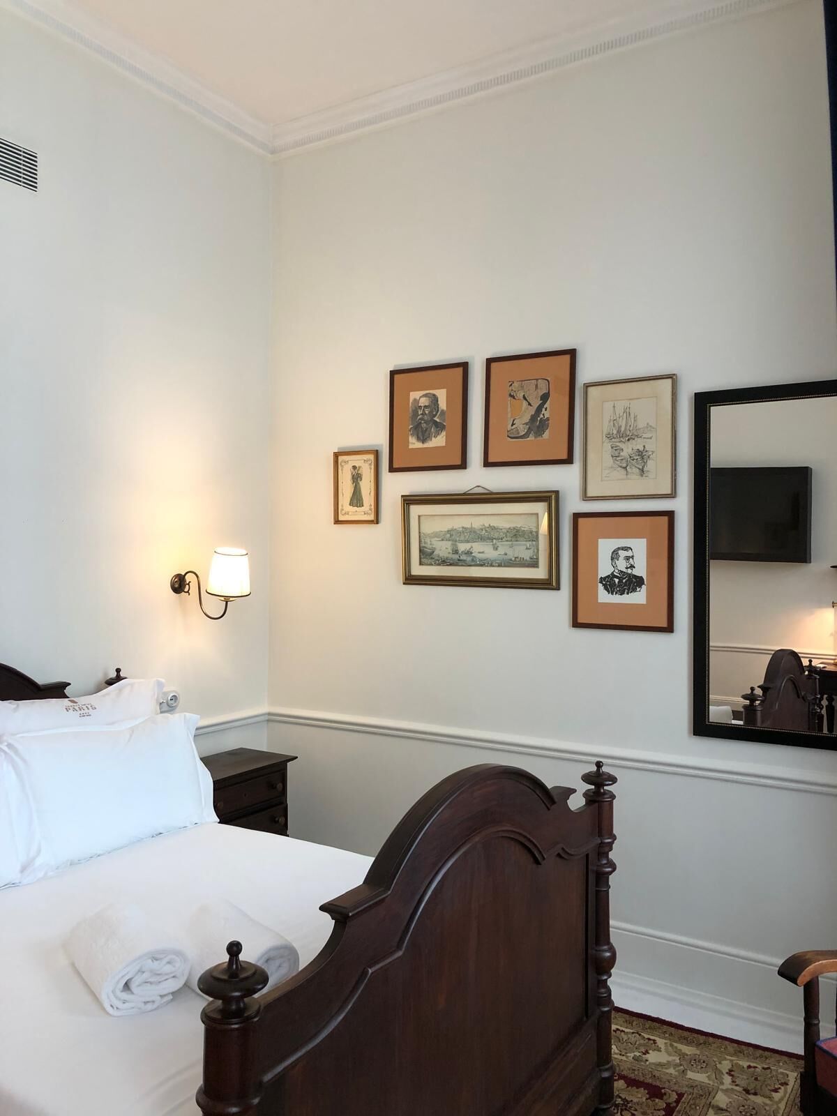 Hotelkamer met een houten bed, nachtkastje, een wandlamp en enkele ingelijste foto's.