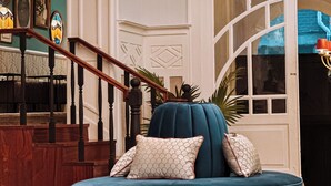 A blue sofa with patterned pillows in a room with a staircase and a large window. - GRANDE HOTEL PARIS by STAY HOTELS (Porto)