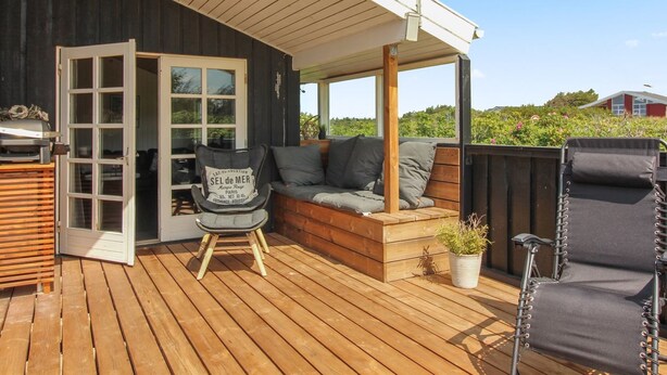 A wooden deck with a sofa, a chair, and a grill.