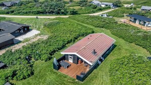 A large house with a red roof and a deck, surrounded by lush greenery and a view of the ocean.