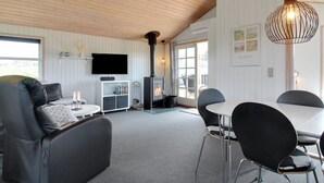 A modern living room with a sofa, a dining table with chairs, a fireplace, and a television mounted on the wall.