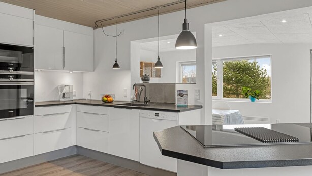 A modern kitchen with white cabinetry, a black countertop, and pendant lighting.