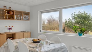 A dining area with a table set for four, a window with a view of trees, and a shelf with decorative items.
