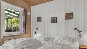 A bedroom with two beds, a window with curtains, a wall-mounted lamp, and signs with city names.