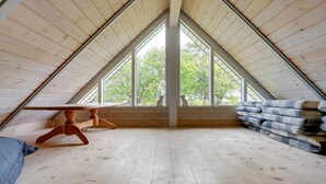 A high-ceilinged attic room with wooden floors, a wooden table, and a large window offering a view of trees. - "Radojka" - 75m from the sea by Interhome (Otterup)