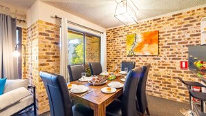 A dining area with a brick wall, a table set for four, and a fire extinguisher sign. - Bay Parklands, 27/2 Gowrie Ave pool tennis court spa and views (Nelson Bay)