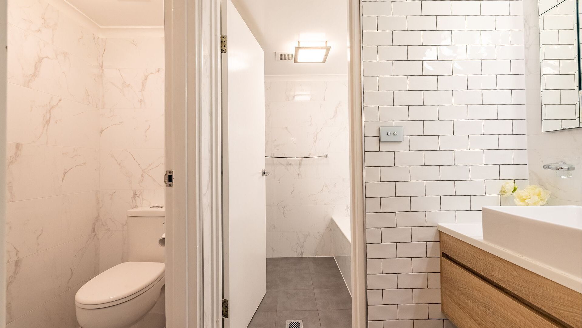 A bathroom with white marble walls, a white toilet, a shower area, and a vanity with a mirror.