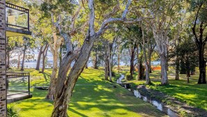 A park with a brick building, trees, and a body of water in the background. - Bay Parklands, 27/2 Gowrie Ave pool tennis court spa and views (Nelson Bay)
