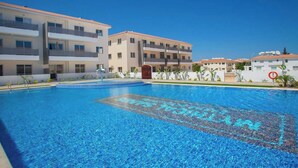 En swimmingpool med ett klart, blått vatten, omgiven av höga byggnader med balkonger och en klar himmel.