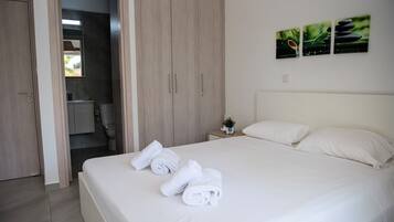 A hotel room with a bed, white towels, a nightstand with a plant, and a wall-mounted artwork.