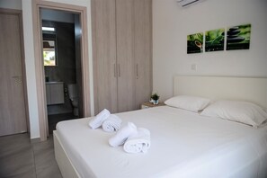 A hotel room with a bed, white towels, a nightstand with a plant, and a wall-mounted artwork. - Carme At The Beach - Mythical Sands Resort (Paralimni)