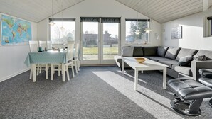 A spacious living room with a high ceiling, a dining area with a table and chairs, a grey sofa, a black leather bench, and a large window offering a view of the outdoors. - "Ingward" - 300m to the fjord by Interhome (Tarm)