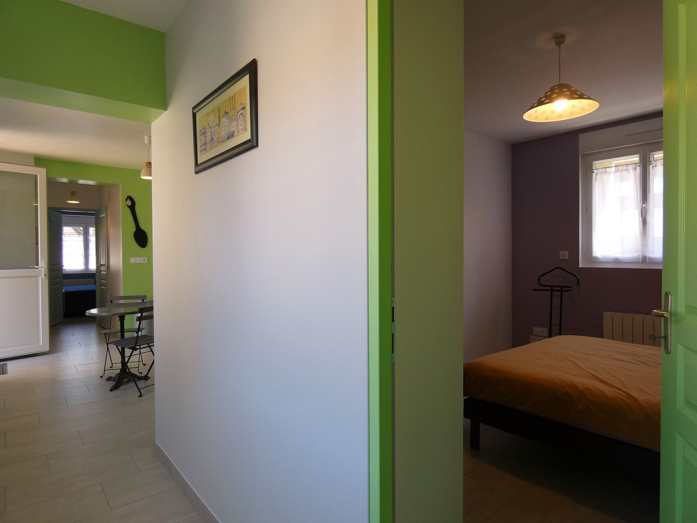 Une pièce avec un lit, une table et une chaise, une fenêtre avec des rideaux et un mur vert.