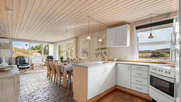 Eine moderne Küche mit Holzboden, weißen Schränken und einem großen Fenster mit Blick ins Freie.