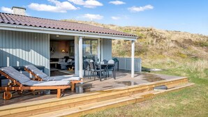 Ein Küstenhaus mit Terrasse, Sitzgelegenheiten im Freien und einer überdachten Veranda.