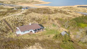 Eine Vogelperspektive eines Küstengrundstücks mit einem Haus, einer unbefestigten Straße und einem Strand im Hintergrund.