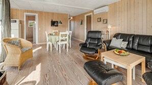 Un salon moderne avec un plancher en bois, un canapé en cuir noir, une table à manger avec des chaises et un fauteuil en osier.