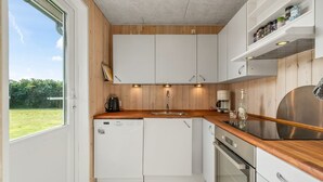 Une cuisine compacte avec des meubles blancs, un plan de travail en bois, un four encastré et une fenêtre donnant sur un espace verdoyant.