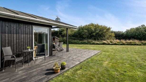 Une maison moderne dotée d’une terrasse en bois, d’un espace salon extérieur et d’une grande porte vitrée donnant sur un patio.