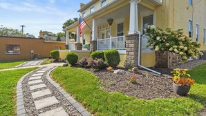 A yellow building with a porch, an American flag, and a well-maintained garden with a stone pathway.