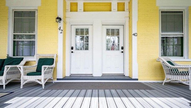 A porch with two white doors, numbered 42 and 40, and two wicker chairs with green cushions.