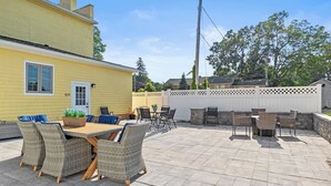 A patio with wicker furniture, a wooden table, and a white fence.