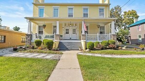 A two-story yellow building with a white front porch, a central entrance, and a flag.