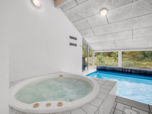 Une piscine intérieure moderne, dotée d’un jacuzzi, de grandes fenêtres et offrant une vue sur l’extérieur.