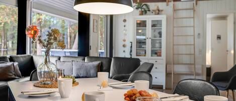 A modern dining area with a long table, white tableware, and a vase with dried flowers.