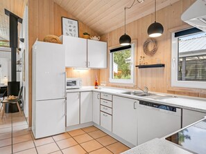 Une cuisine moderne avec des meubles blancs, un four à micro-ondes, un lave-vaisselle et une fenêtre donnant sur un espace verdoyant.