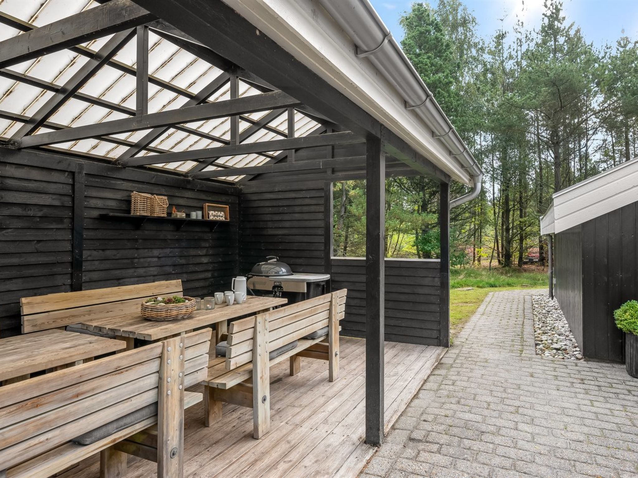 A covered outdoor seating area with wooden benches and a grill.