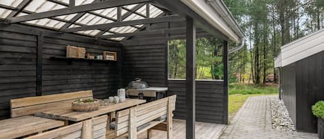 A covered outdoor seating area with wooden benches and a grill.