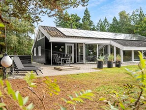 Une maison moderne dotée d’un patio couvert, d’un espace salon extérieur et d’un jardin.