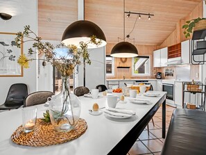 A modern kitchen with white cabinets, a dining area with a long table set for breakfast, and pendant lighting. - "Jensen" - 700m to the fjord by Interhome (Oksbøl)