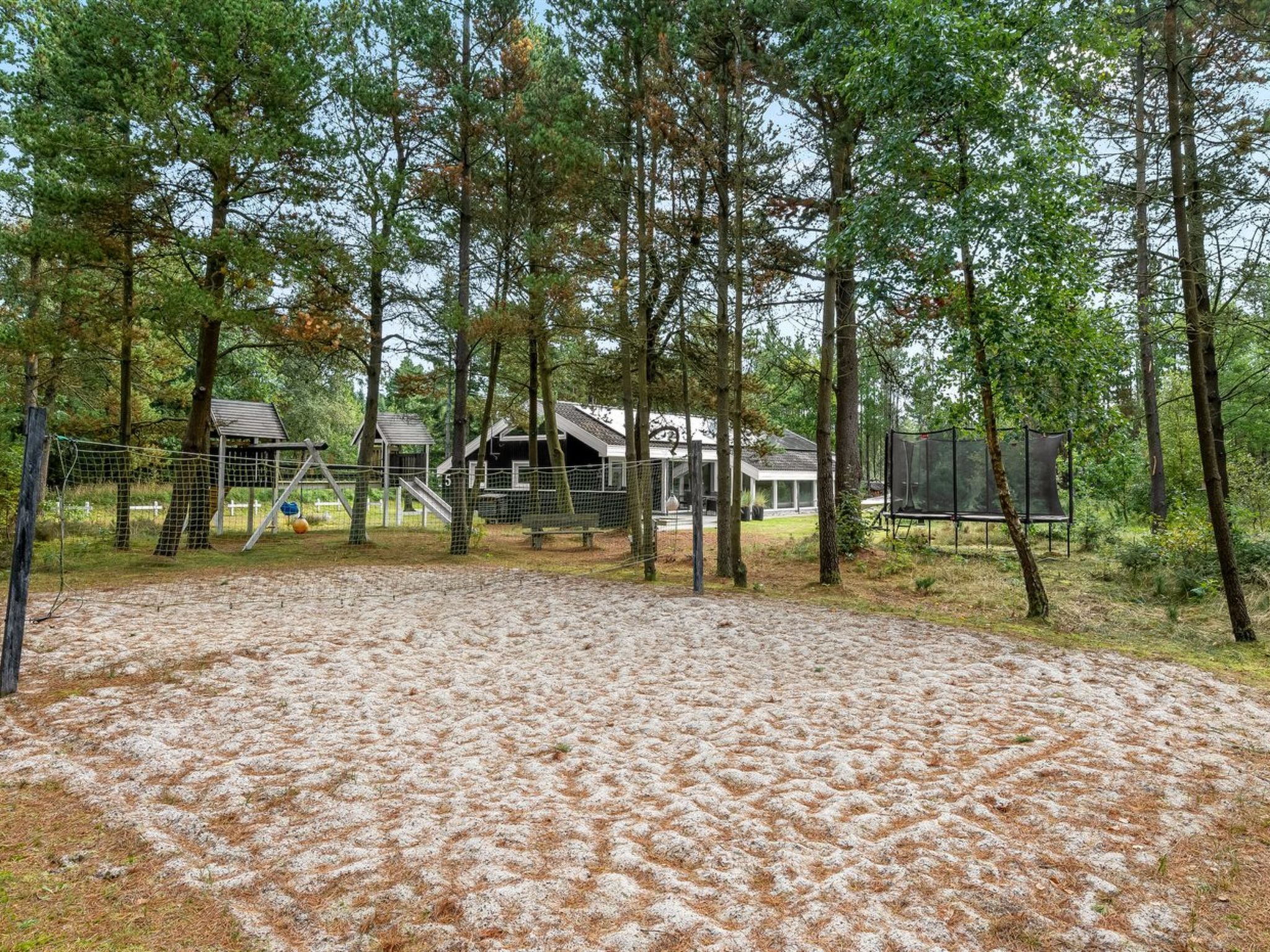 Een bebost gebied met een omheind sportterrein, een klein gebouw en een bank.