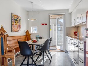 Eine moderne Küche mit weißen Schränken, eine Essecke mit einer hölzernen Bank und schwarzen Stühlen sowie ein farbenfrohes abstraktes Gemälde an der Wand.