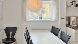 A modern dining area with a white table and black chairs, a hanging light fixture, and a window with curtains.