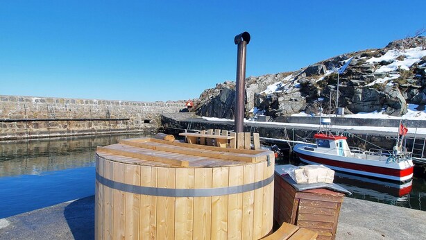 A wooden sauna structure with benches and a chimney, located near a dock with a boat.