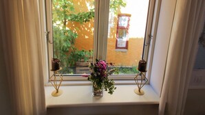 A window with two small tables holding candles and a vase of flowers.