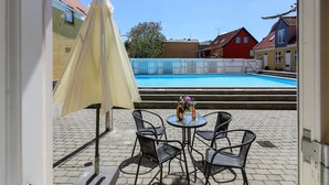 A view of a swimming pool with a white fence, a yellow umbrella, and outdoor seating with chairs and a table.