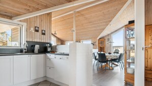 Une cuisine moderne avec des meubles blancs, un plan de travail noir et un îlot central. On aperçoit un coin repas avec une table et des chaises à travers une porte ouverte.