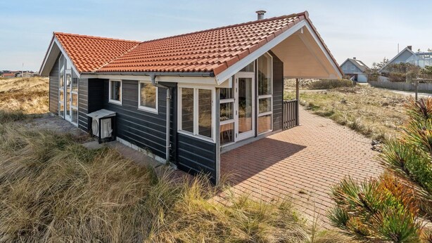 Une maison située sur la côte, avec un toit recouvert de tuiles rouges, de grandes fenêtres et un chemin en briques menant à l’entrée.