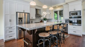 A modern kitchen with white cabinetry, stainless steel appliances, a granite countertop, and bar stools.
