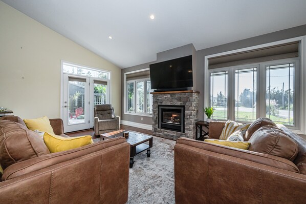 A living room with a stone fireplace, leather sofas, and large windows.