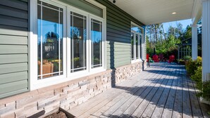 A covered wooden deck with brick accents, large windows, and red chairs.
