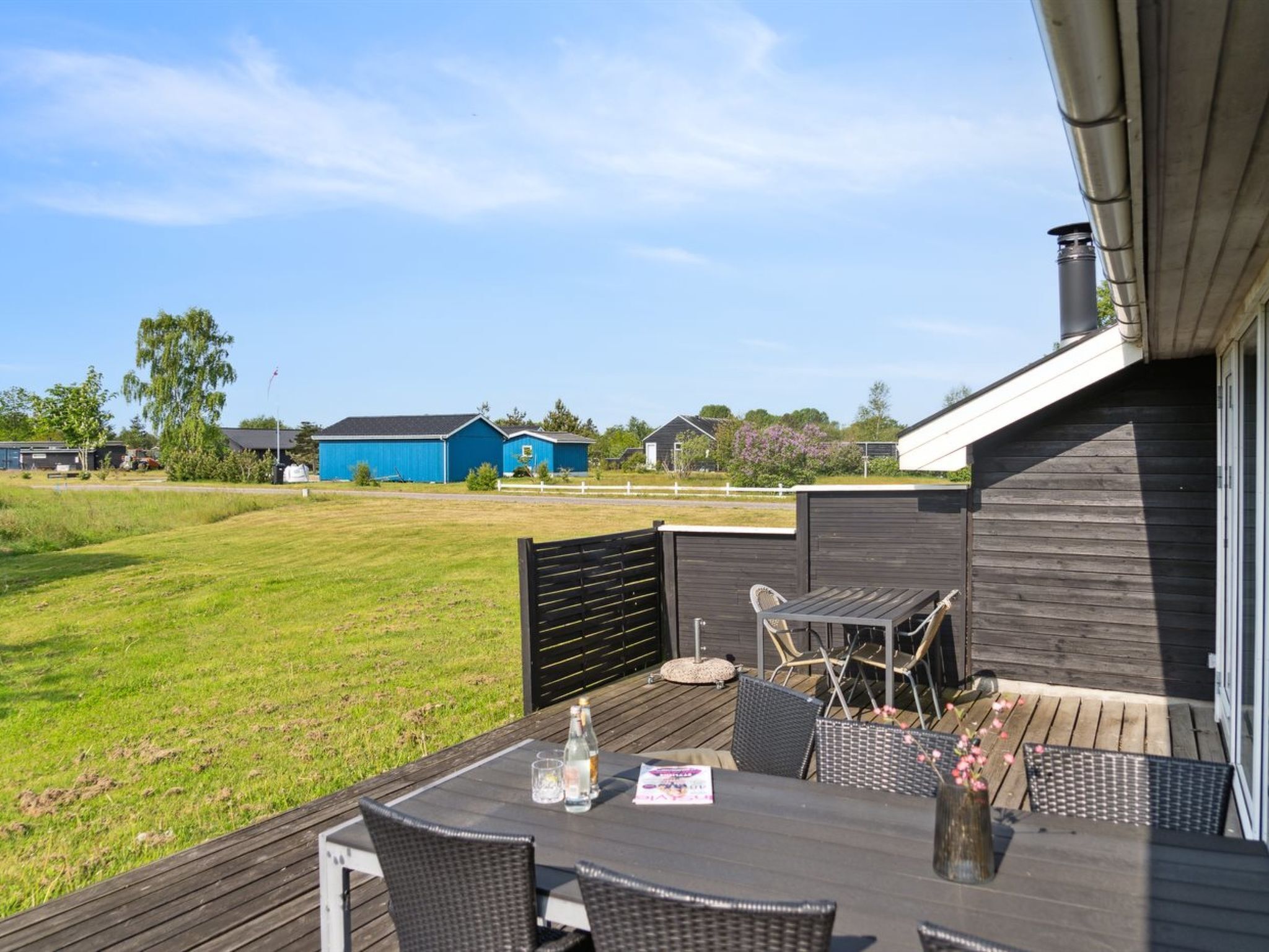 Une terrasse avec une table et des chaises, une plateforme en bois et une vue sur une grange bleue et un champ verdoyant.