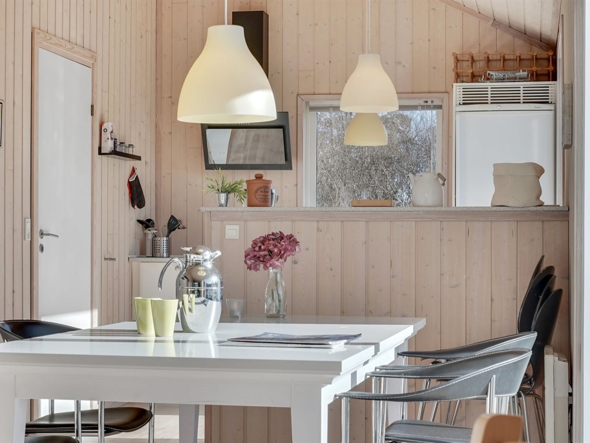 Eine moderne Küche mit Holzvertäfelung, Pendelleuchten, einem weißen Tisch und Barhocker.