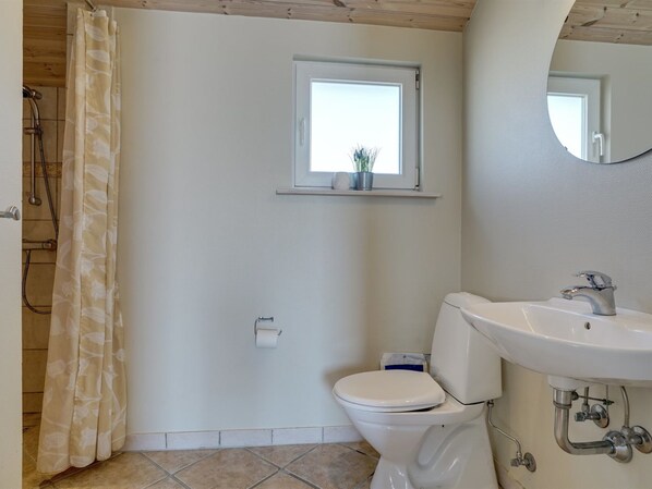 A bathroom with a toilet, sink, shower, and a window above the toilet.