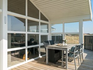 A modern outdoor dining area with a table and chairs, large windows, and a view of the landscape.