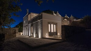 A modern building with a stone facade, a large illuminated entrance, and a paved courtyard.